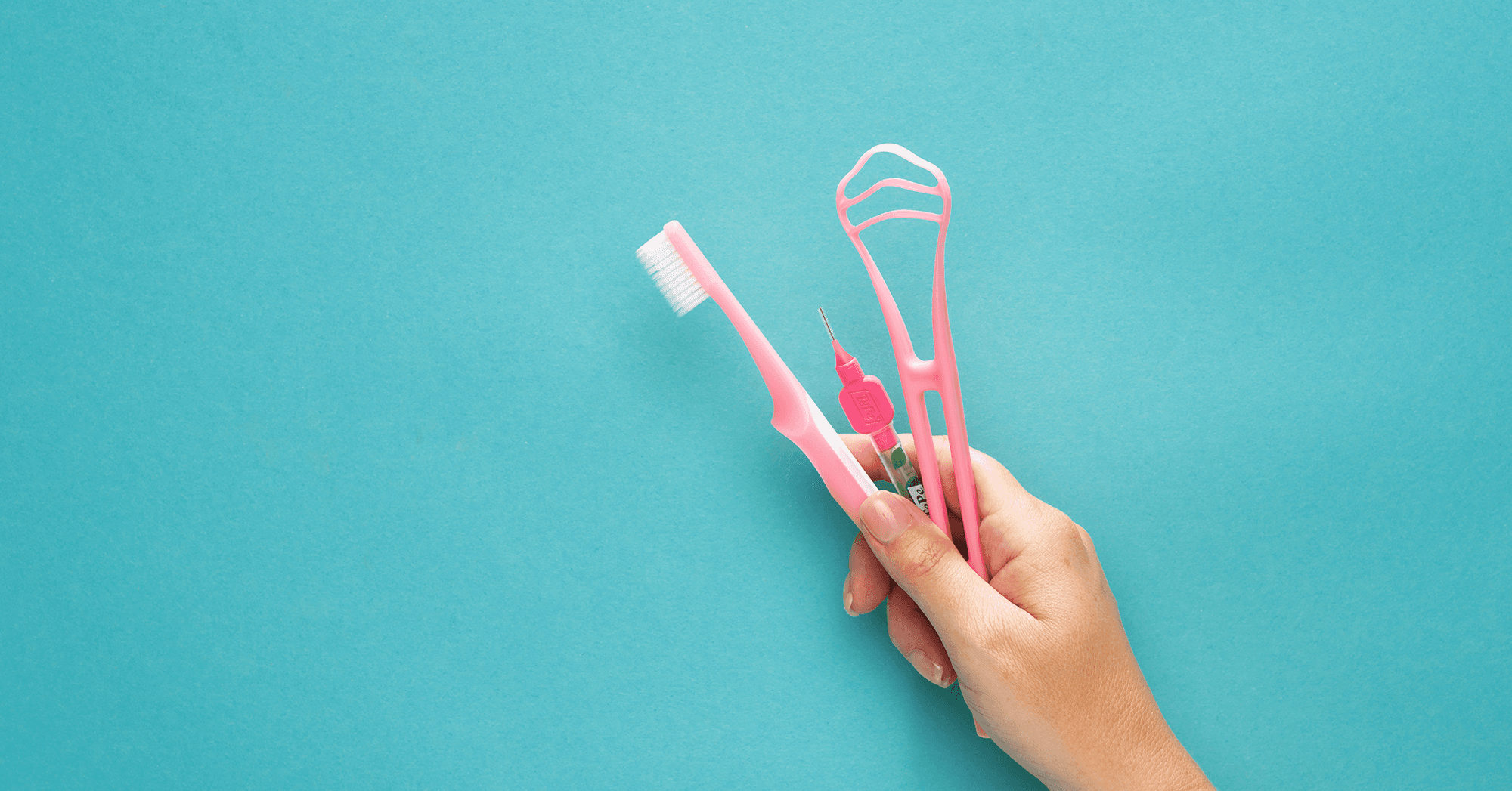 Hand holding a toothbrush, interdental brush and tongue scraper from TePe