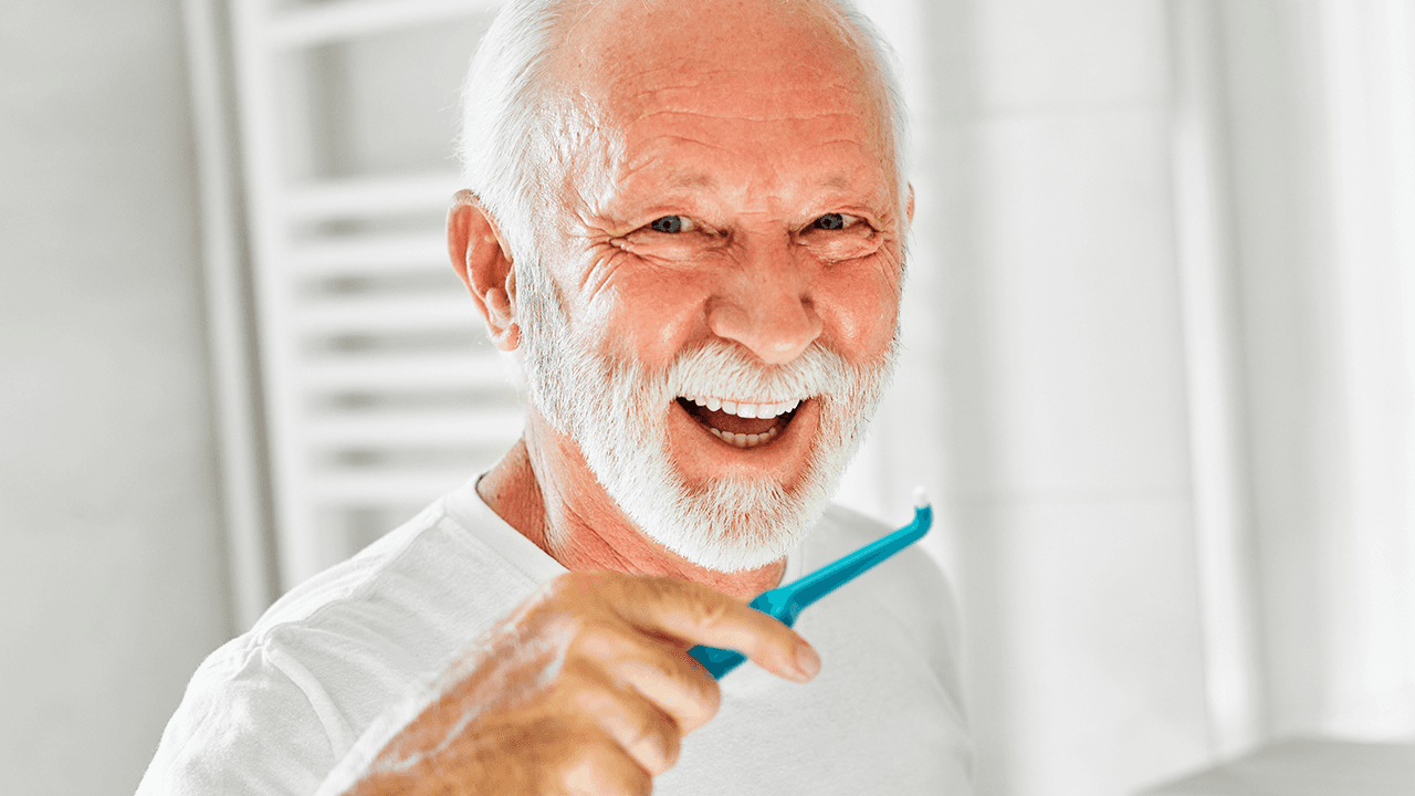 older man using a TePe Compact Tuft to clean his implants
