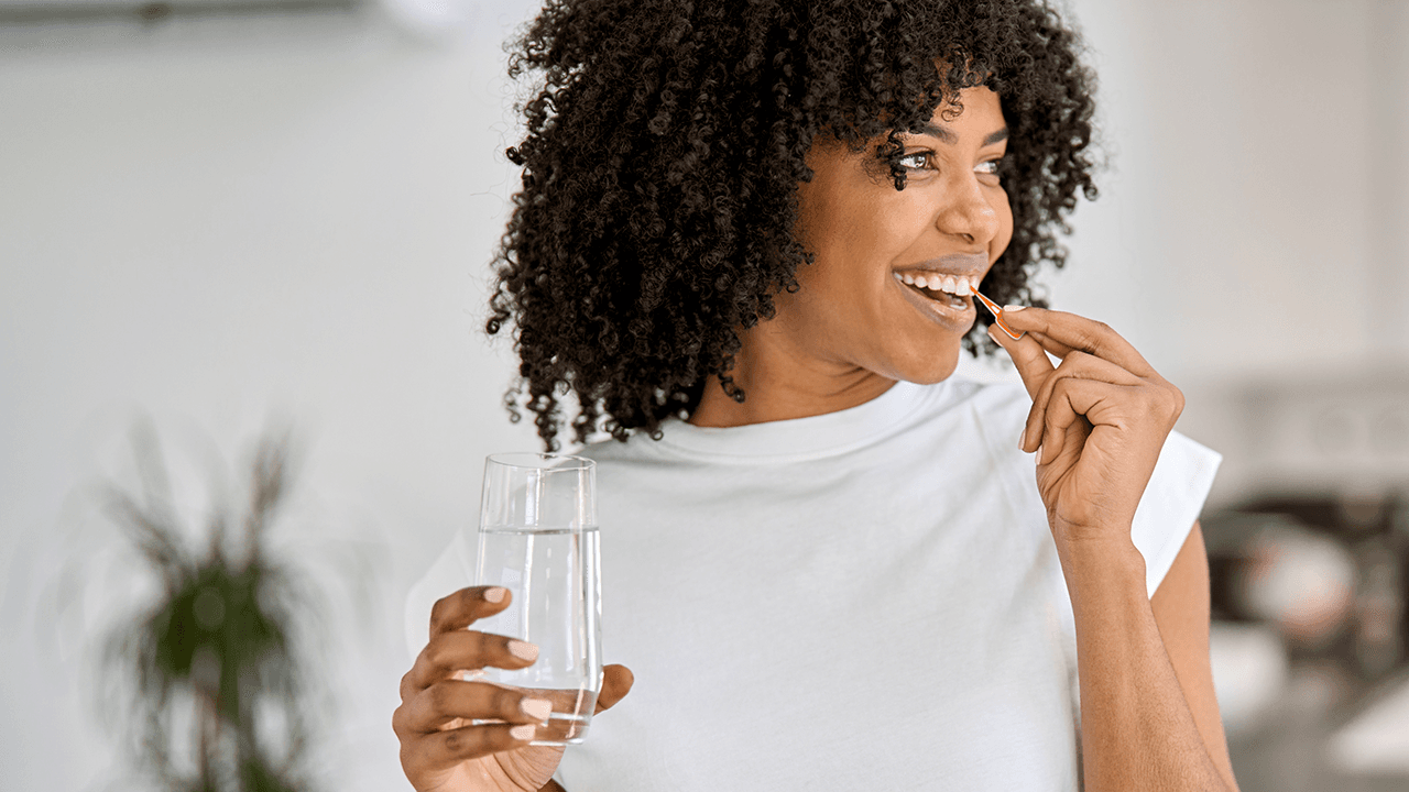 Woman holding a glass of water as she cleans between her teeth with a TePe EasyPick